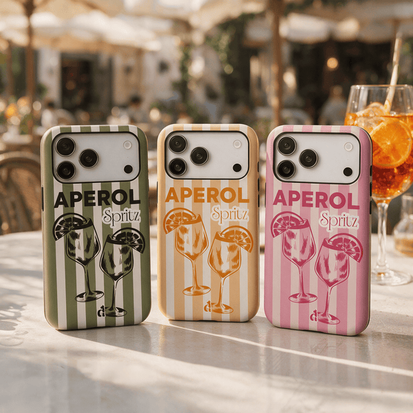 Trois coques de téléphone premium Aperol Spritz roses, vertes et jaunes sur une table de restaurant. Collection Dolce Vita. Dealer de Coque.